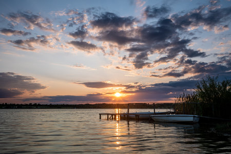 Two fishing boats next to a wooden pier during sunset on Lake Paljuvi in Serbia.の写真素材