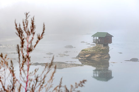 A small wooden house on a rock surrounded by fog in the middle of river Drina in Bajina Basta, Serbia.の写真素材