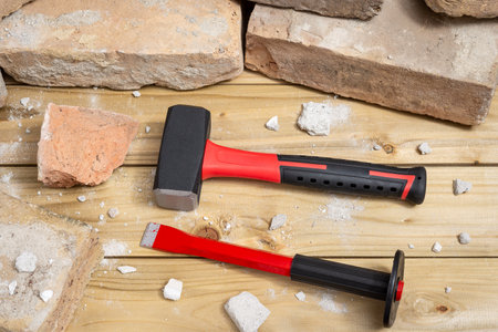 Sledgehammer with chisel next to an old brick on a wooden table. Selective focus.