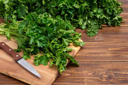 Cutting board with bunch of fresh parsley and kitchen knife on a wooden table with copy space for text. Selective focus.の写真素材