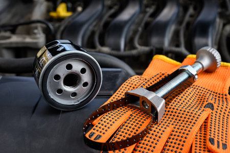 New oil filter with adjustable tool for removing oil filters in a car and protective gloves under the open hood of car. Selective focus.の写真素材