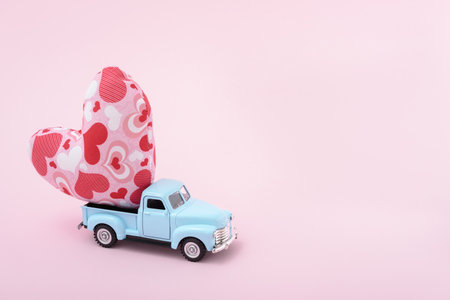 Blue retro toy car delivering heart for Valentine's day on pink background. Valentine's Day conceptの写真素材