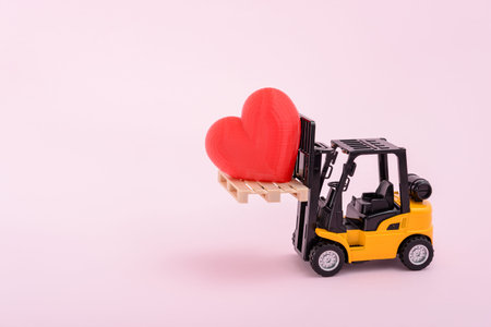 A forklift lifts a red heart on a light pink background with copy space for text.の写真素材