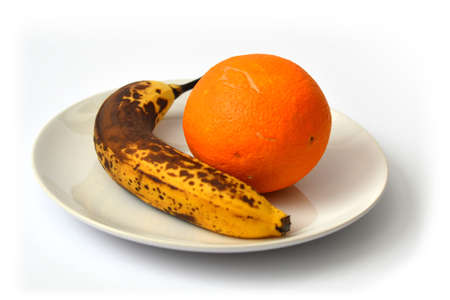 Overripe banana and orange on the plate on white backgroundの写真素材