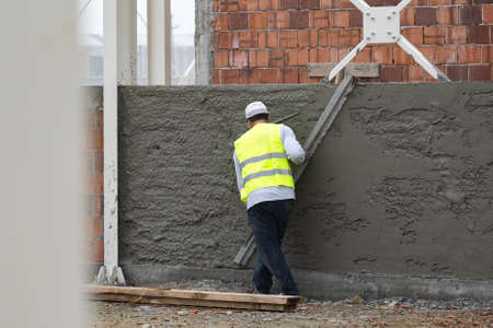 Worker in a reflective jacket leveling a plaster wall in a construction siteの写真素材