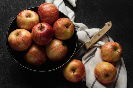 Apples in a bowl on a black table with a knife. Red and yellow shiny apples on a kitchen cloth