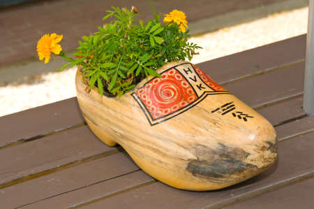 AMSTERDAM, HOLLAND - JULY 18, 2010: Dutch wooden clog with red motifs painted and yellow flowers inside, photographed in the street.のeditorial素材