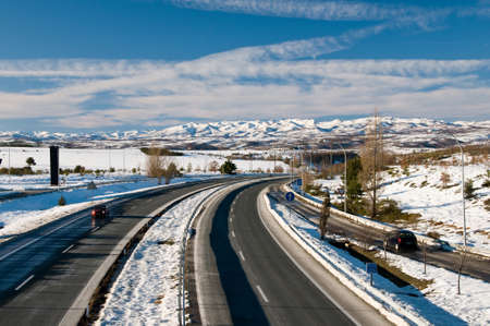 RIOSECO DE TAPIA, SPAIN - DECEMBER 21, 2008: Cantabrian Mountains view from Rioseco de Tapia. Leon. Spain. Highway mountain valley and snow capped mountains. Nice picture. Snow. Deep blue sky with clouds. A few cars on the highway.のeditorial素材
