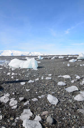Blue skies with chunks of glaciers on a black sanded beach 