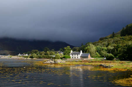 Dark skies in Kyle of Lochalsh with a cute house on the shore の写真素材