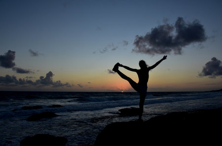Silhouetted to hold bind balance pose at sunrise along the coast.