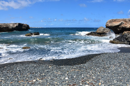 Waves coming ashore on the black stone beach on the coast of Aruba.の写真素材