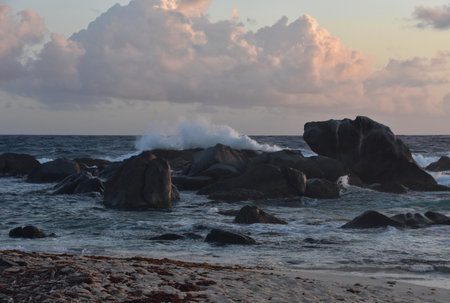 Large waves crashing on rock formations in the ocean under pink clouds.
