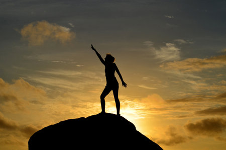Woman reaching for the sun as it rises up over the horizon.の写真素材
