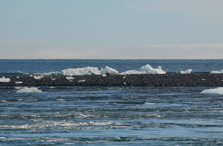 Chunks of ice scattered across a black sandbar in the ocean off of Iceland