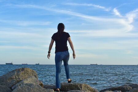 Girl standing on a rock at the seashore Look at the beautiful sky