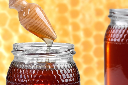 two jars of honey, and wooden drizzler on honeycombs background の写真素材