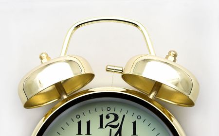 Gold alarm clock, very loudly ringing, showing 12 pm.