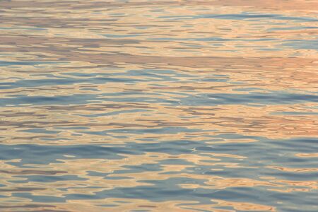 Rippled golden sea surface with reflections of sunrise.の写真素材