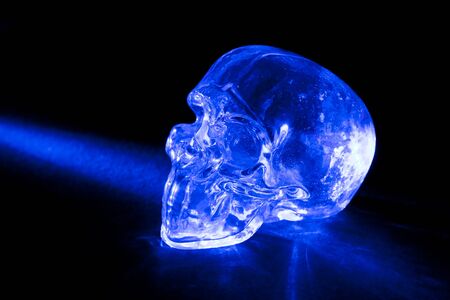 Transparent glass skull with blue light ray against black background.の写真素材