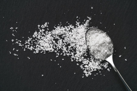 Organic sea white salt and a spoon on a black slate stone background. Concept of cooking natural healthy food.の写真素材