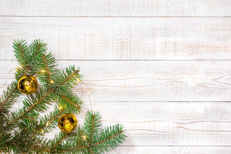 Christmas background - fir branches with golden decorations and light garland on a white wood table. Flat layout, top view composition border with copy space.の写真素材