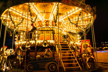 Vivid evening scene of a classic carousel with zebras and horses, bright lights, and striped canopy at a festive European Christmas market in Germany.の写真素材