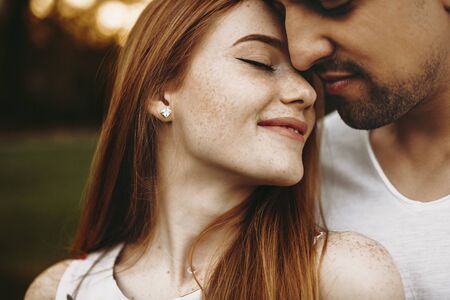 Amazing red hair girl with freckles leaning her head on her boyfriend head smiling with closed eyes against amazing sunset light outside while traveling.の写真素材