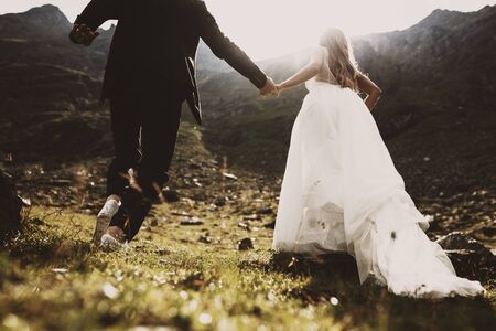 Crop view of legs of groom and bride running up on the mountains against sunset by holding hands. Running to family life.の写真素材
