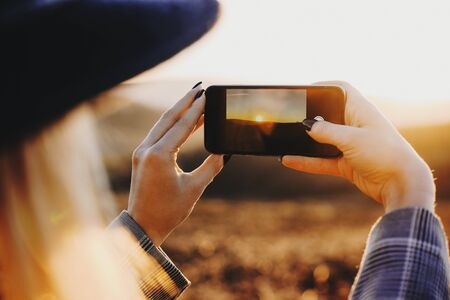 Young blonde female traveler taking a picture of an epic sunset while traveling in her spring vacation time.の写真素材