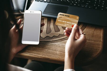 Female hands using a credit card and a smartphone for playing online while sitting at a table in a...