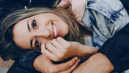 Charming caucasian lady with a cheerful toothy smile is lying on her boyfriend being embraced by him