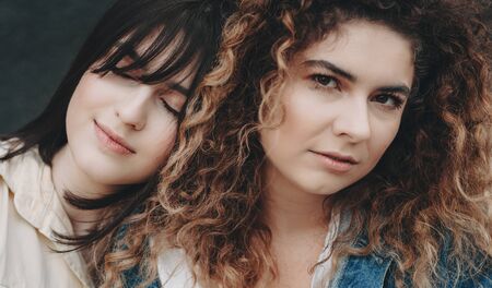 Close up photo of a curly caucasian girl looking at you and her brunette sister leaning on her with...