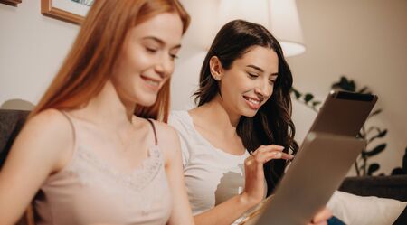 Two beautiful caucasian ladies are using their gadgets while smiling cheerfully and relaxing from...