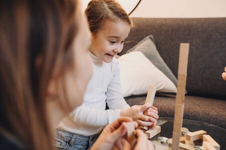Cute girl dressed in a white sweater is playing happily board games with her caucasian mother