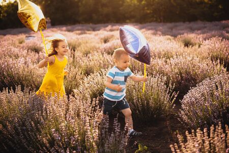 Lovely caucasian kids running against the sunshine with some balloons through a lavender fieldの写真素材