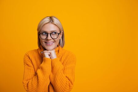 Charming caucasian blonde girl is looking aside through her eyeglasses holding her hand near the...