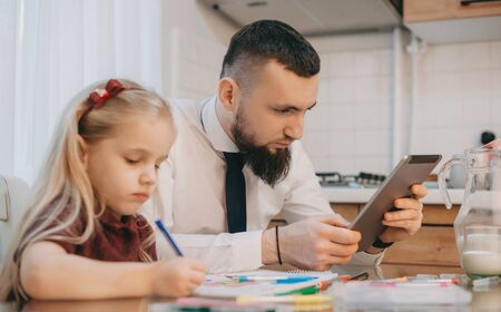 Caucasian man with nice beard is looking at his gadget while a blonde girl near him is writing...