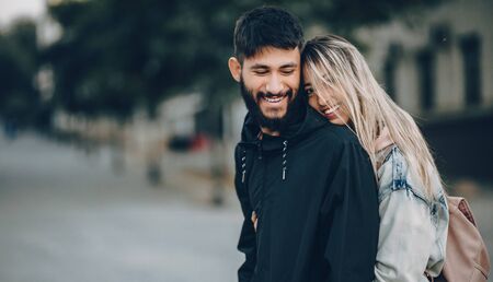 Handsome bearded boy being embraced by his caucasian blonde girl while walking and smiling cheerfullyの写真素材