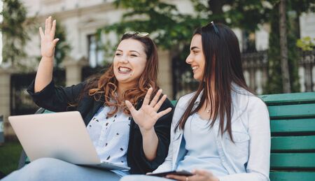 Charming plus sized woman telling future plans to her caucasian sister with black hair and nice smile sitting on a bench in parkの写真素材