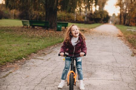 Lovely caucasian girl riding the bike and smiling cheerfully during an autumn walking in the parkの写真素材