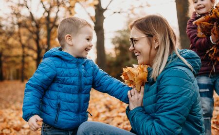 Cheerful caucasian mother playing with her kids while they are bringing autumn colorful leavesの写真素材