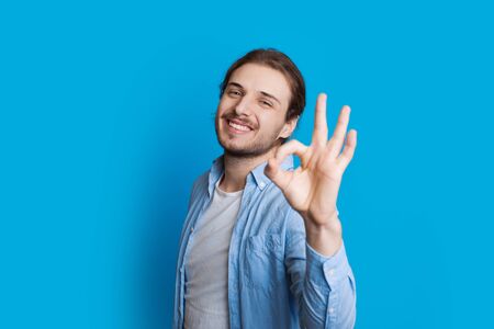 Handsome caucasian boy gesturing approbation sign while smiling and posing on a blue backgroundの写真素材