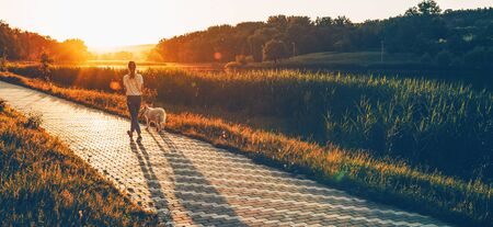 Back view of a caucasian girl running in the park with her dog against the sunshine