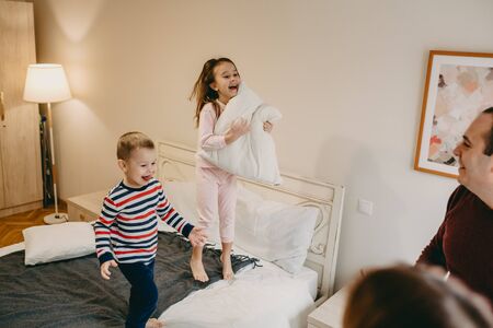 Lovely Caucasian girl holding a pillow and playing with her younger brother while her parents are watching themの写真素材