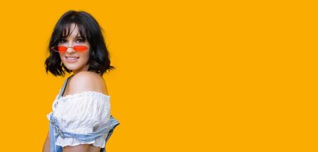 Gorgeous black haired caucasian lady is posing and smiling on a yellow blank spaced background...