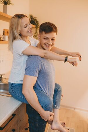 Charming blonde girl embracing her lover while sitting in the kitchen and spending time togetherの写真素材