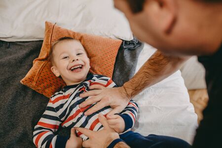 Upper view of a caucasian father tickling his small son who is looking at camera and smiling with...