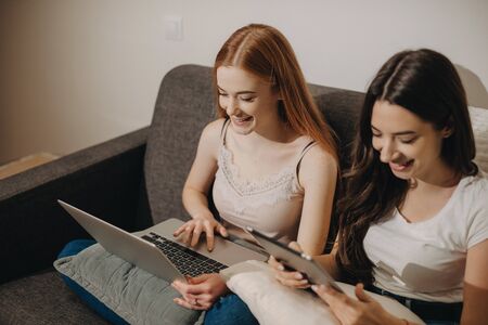 Upper view portrait of two concentrated smiling girls with nice hairs using a laptop and tablet during a summer dayの写真素材