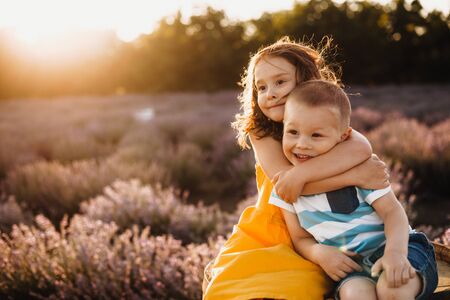 Careful sister embracing her small brother while posing against the sunshine with a lavender field on backgroundの写真素材
